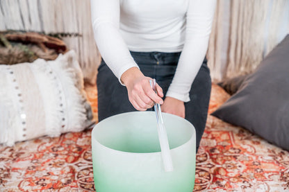 Person playing a green frosted crystal singing bowl for sound healing
