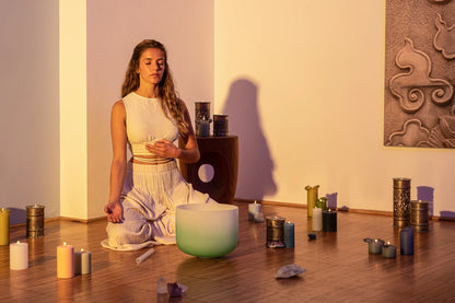 Woman meditating with crystal singing bowl, candles, and crystals in a sound healing room