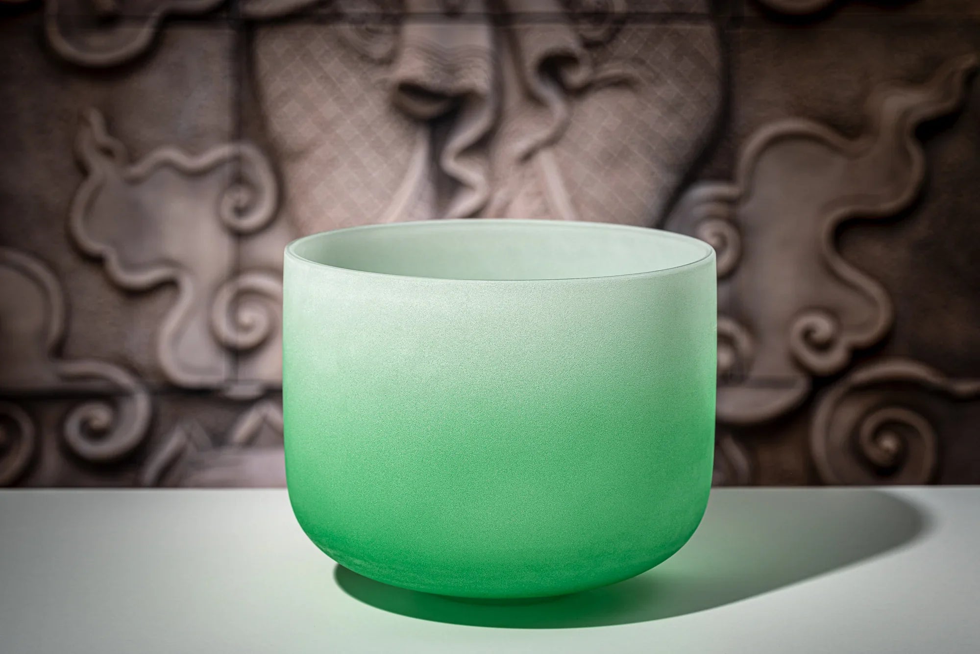 Green frosted crystal singing bowl for sound healing on decorative background