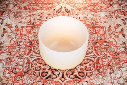 White crystal singing bowl on a patterned red and beige rug for sound healing