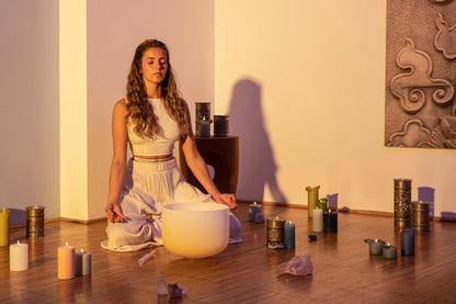Woman meditating with a crystal singing bowl, candles, and crystals in a peaceful room