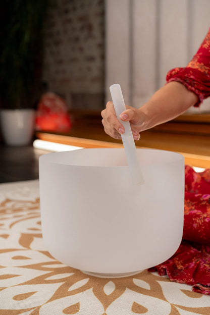Hand playing a white crystal singing bowl with a mallet on a decorative mat for sound healing