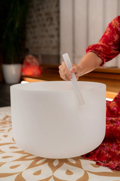 Person playing a frosted crystal singing bowl with a mallet in a serene indoor setting