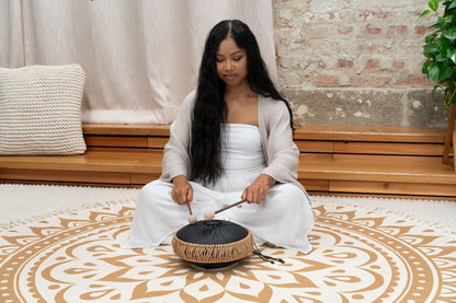 Woman playing a black steel tongue drum with mallets in a peaceful meditation space