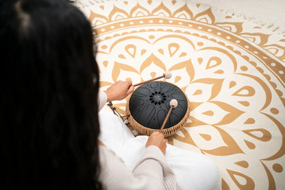 Person playing a black tongue drum with mallets on a patterned mandala mat