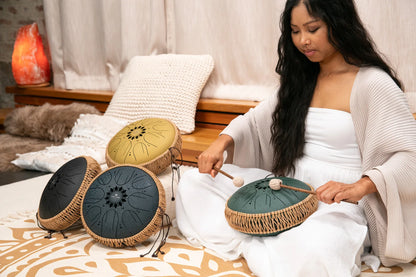 Woman playing steel tongue drum for sound healing in cozy indoor setting
