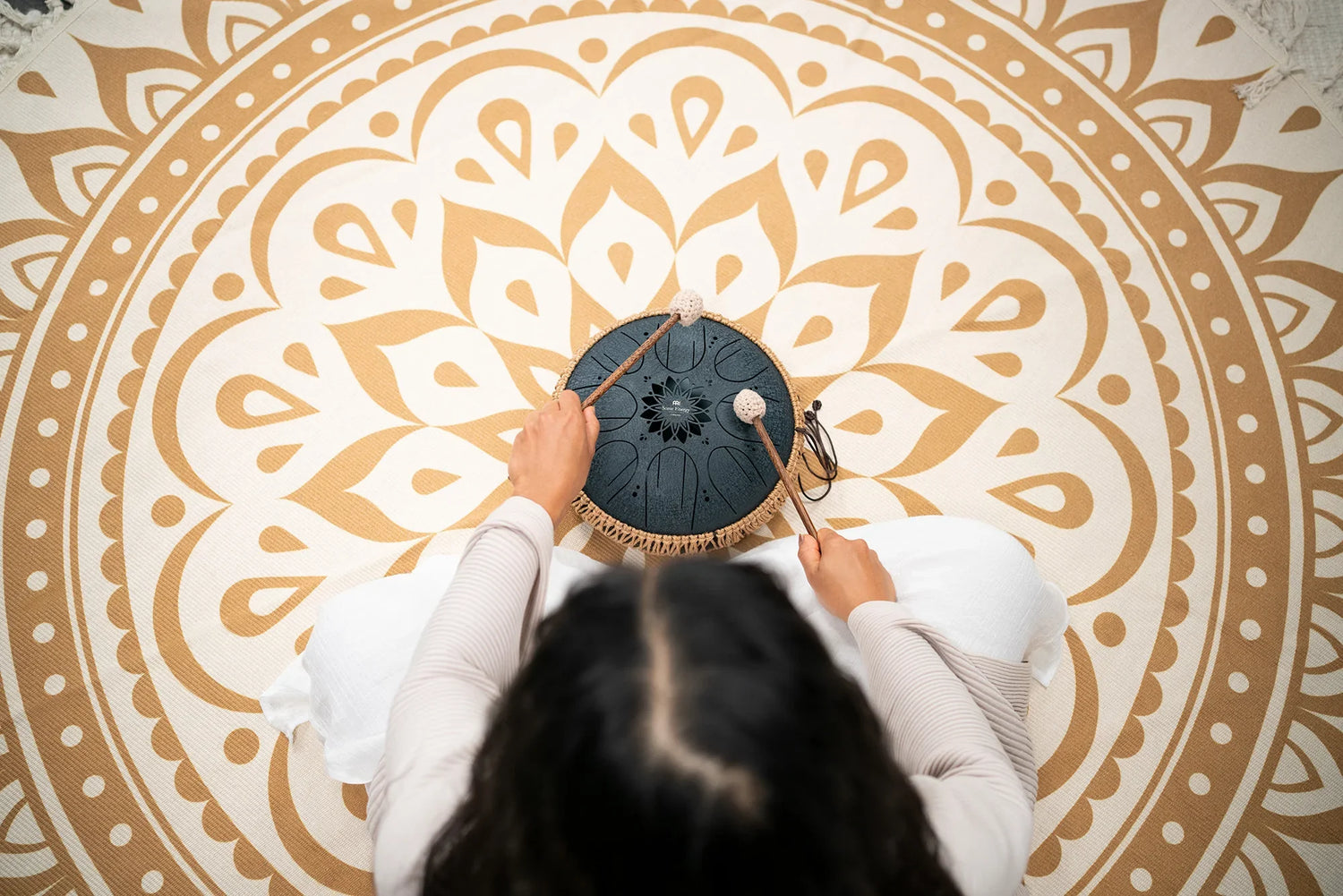 Person playing a steel tongue drum on a mandala mat for sound healing meditation
