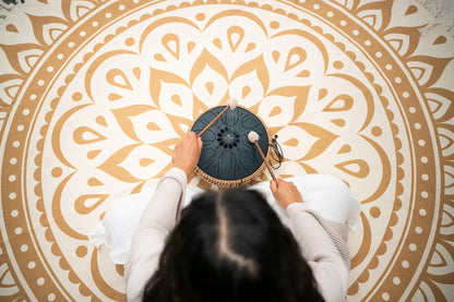Person playing a steel tongue drum on a mandala mat for sound healing meditation