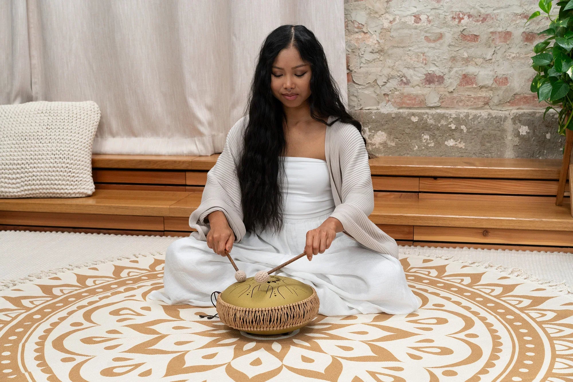 Woman playing handpan drum for sound healing meditation in a peaceful room setting