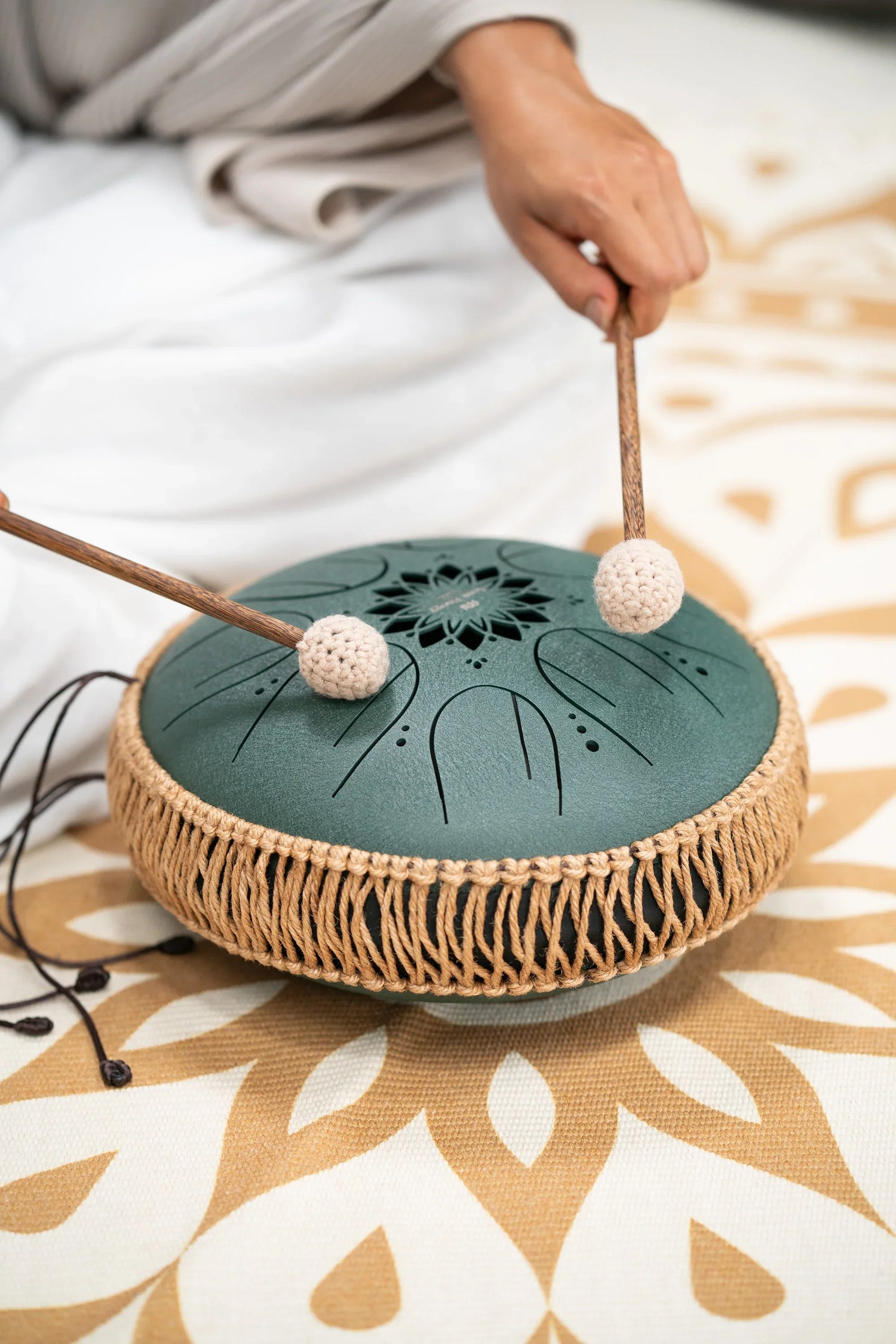 Person playing a steel tongue drum with mallets, used for sound healing and meditation.