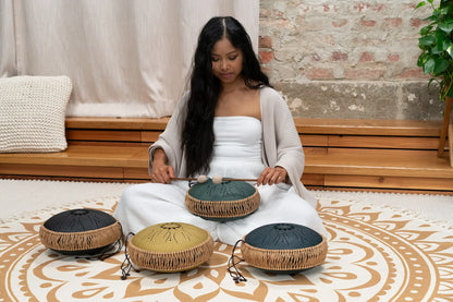 Woman playing steel tongue drums for sound healing on patterned mat in peaceful room