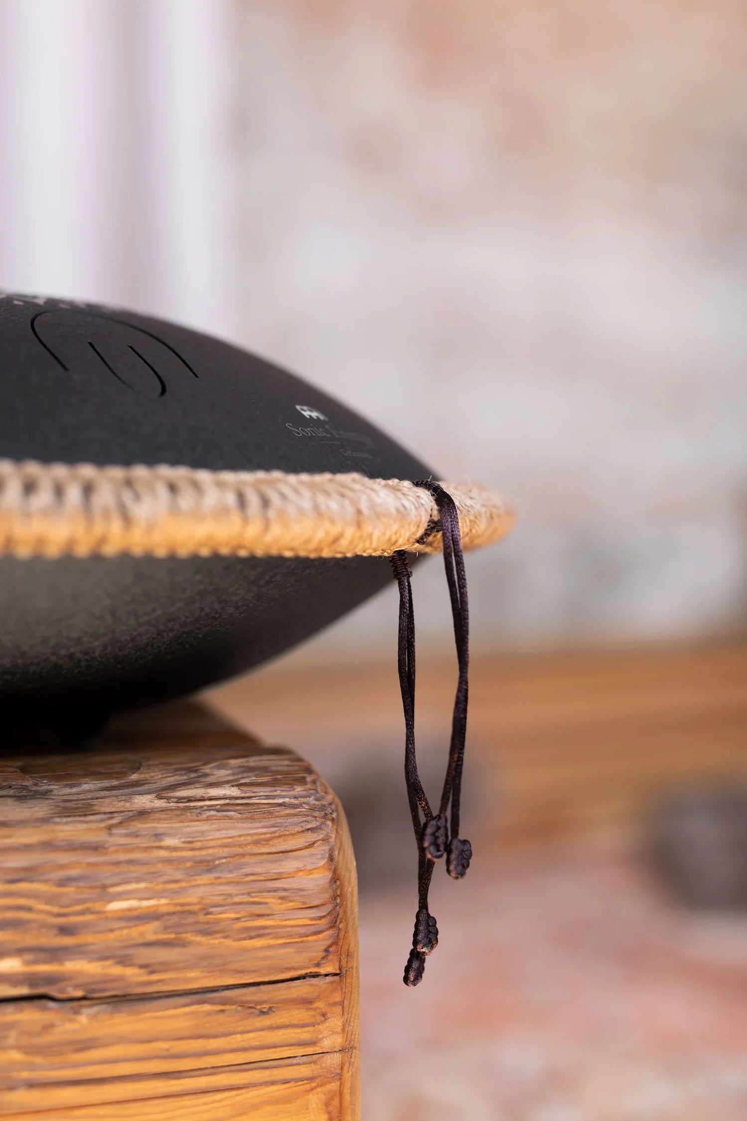 Close-up of a black steel tongue drum with rope edge on rustic wooden surface