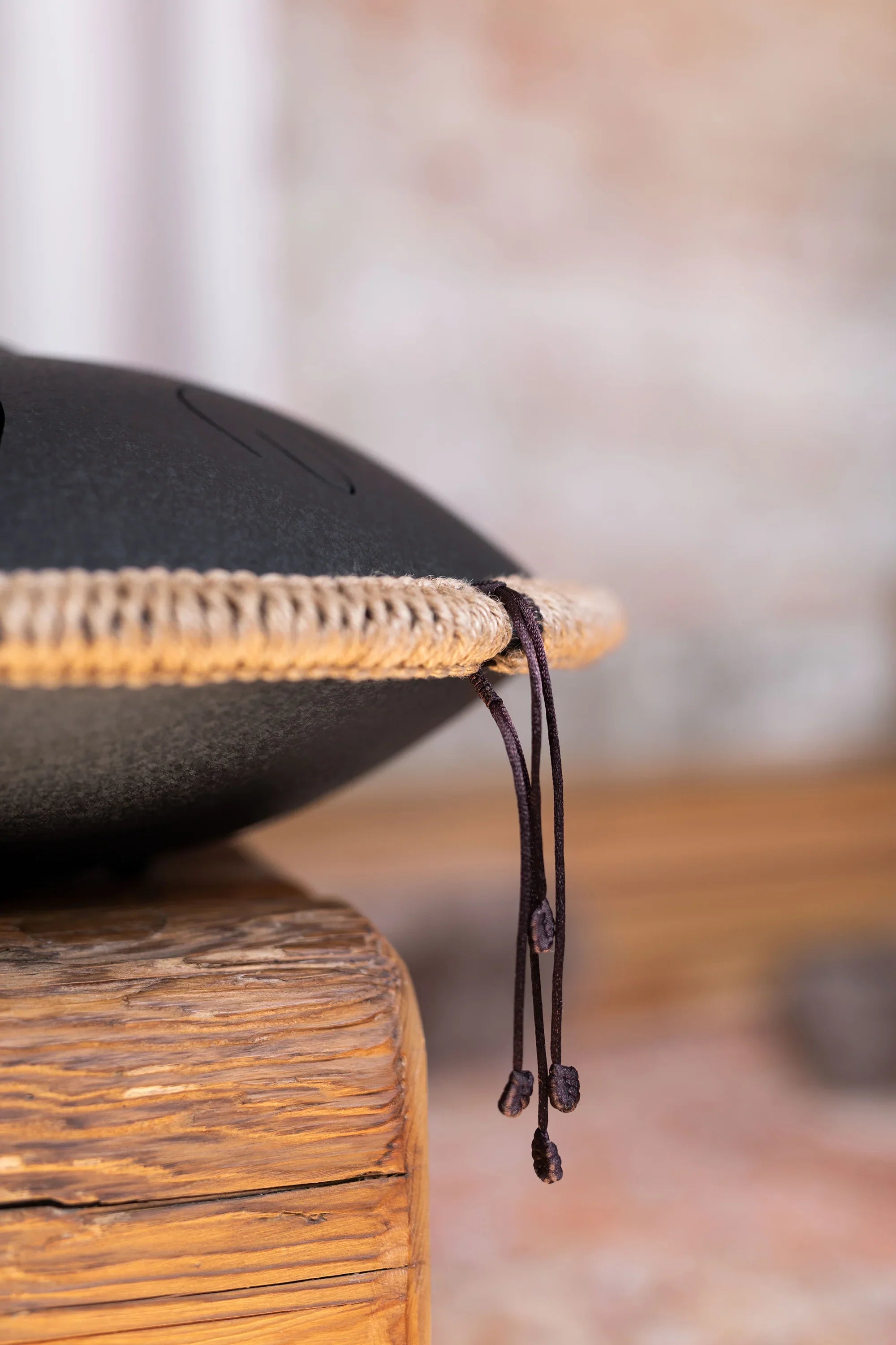Close-up of a black steel tongue drum with rope trim, resting on a rustic wooden surface