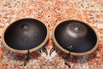 Two black steel tongue drums with mandala and plain designs on patterned rug