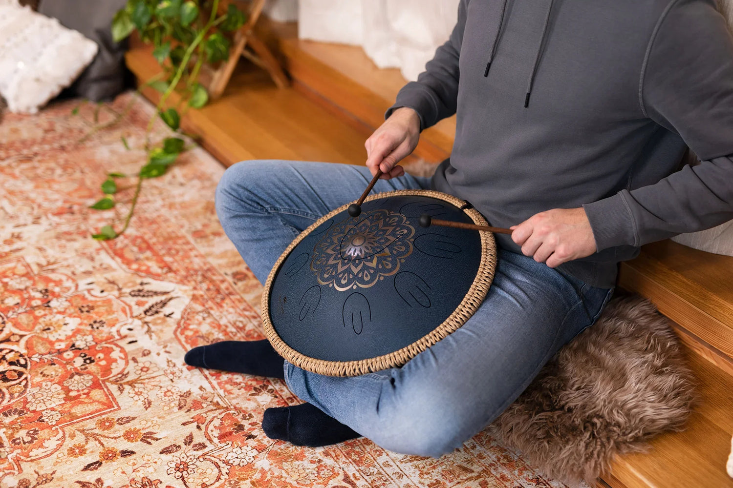 Person playing a handpan drum for sound healing on a patterned rug indoors