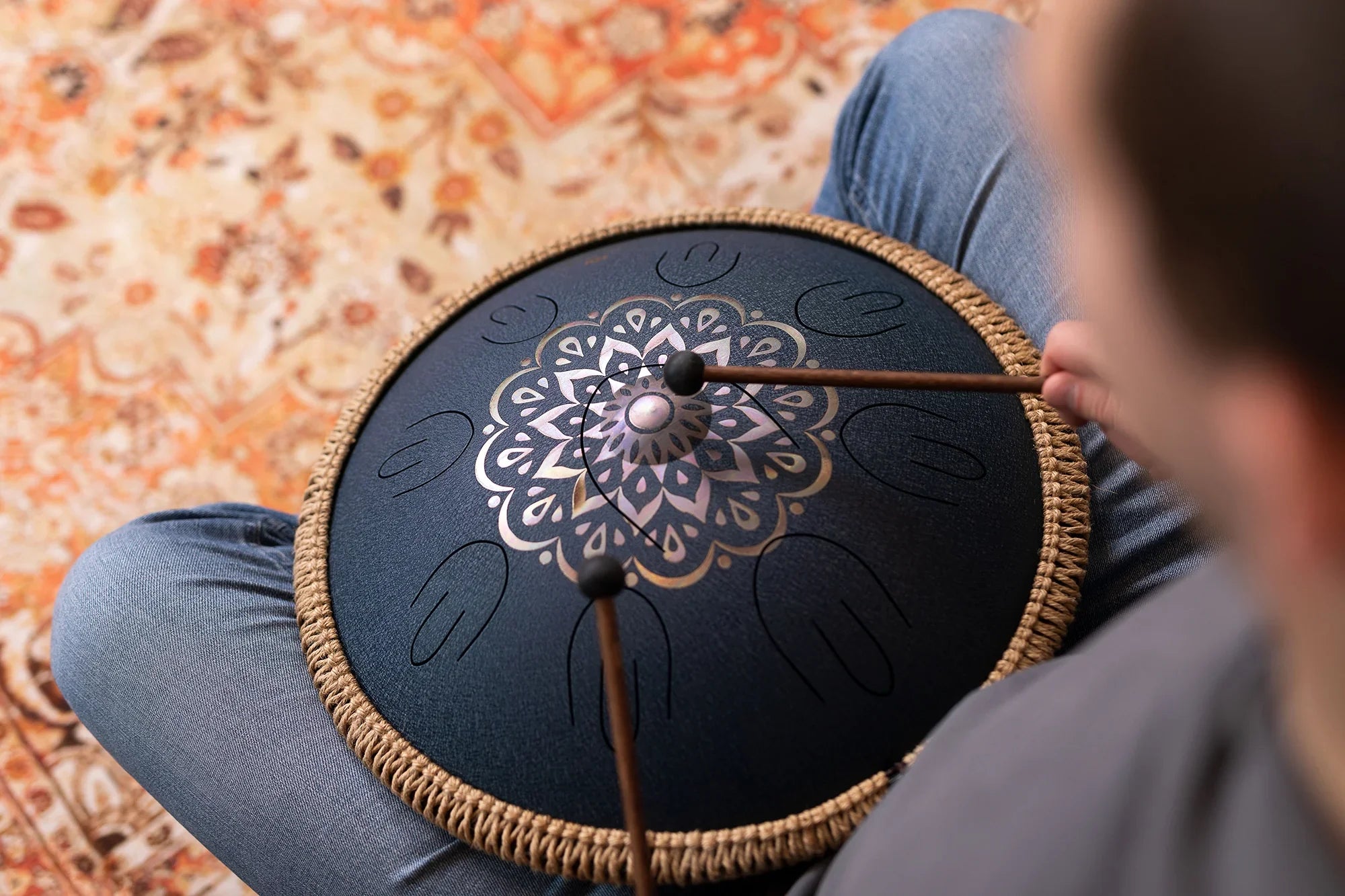 Person playing decorative steel tongue drum with mallets for sound healing