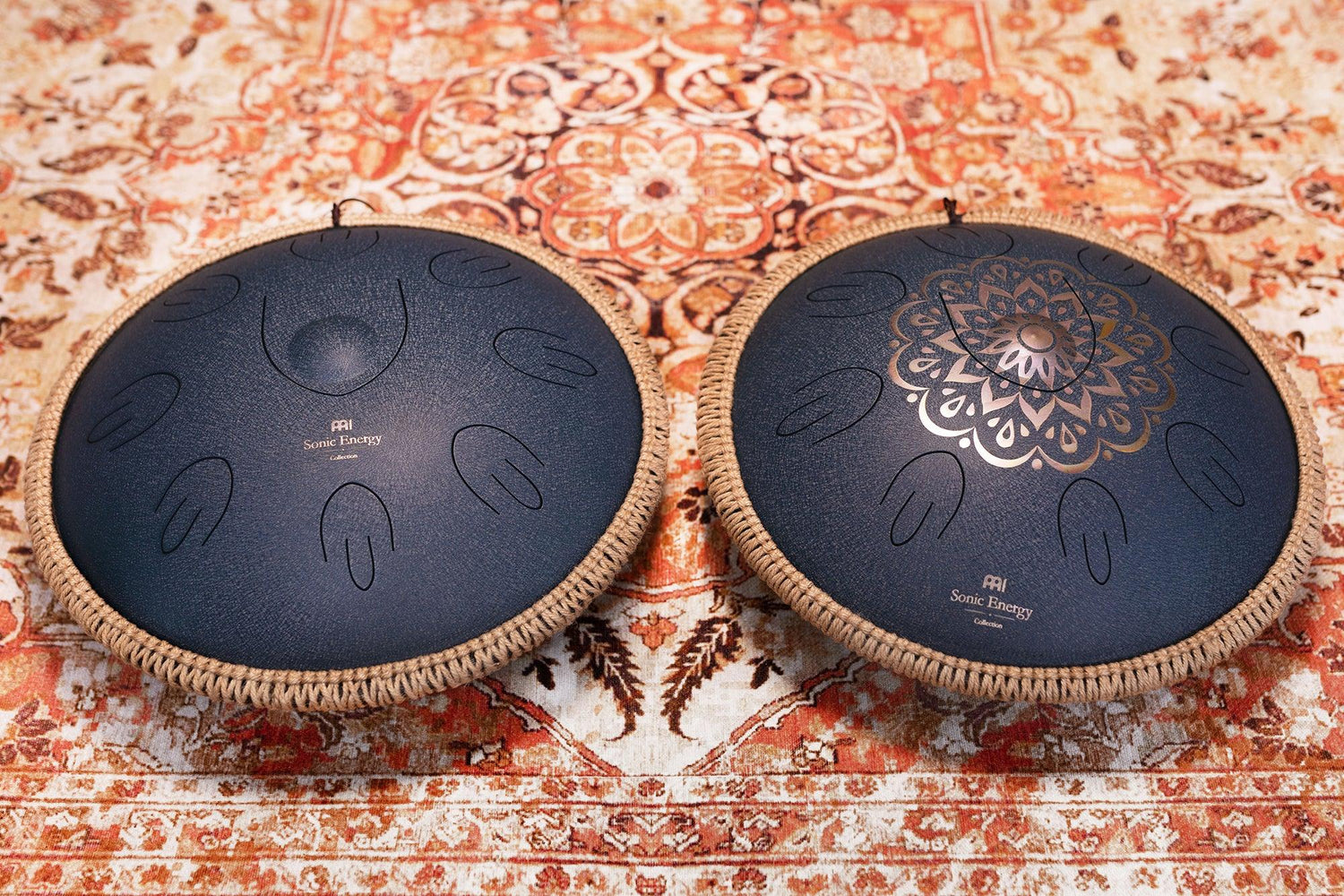 Two black steel tongue drums with decorative edges on a patterned rug, sound healing instruments