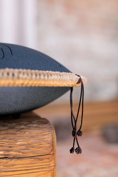 Close-up of a steel tongue drum with rope trim on a rustic wooden surface