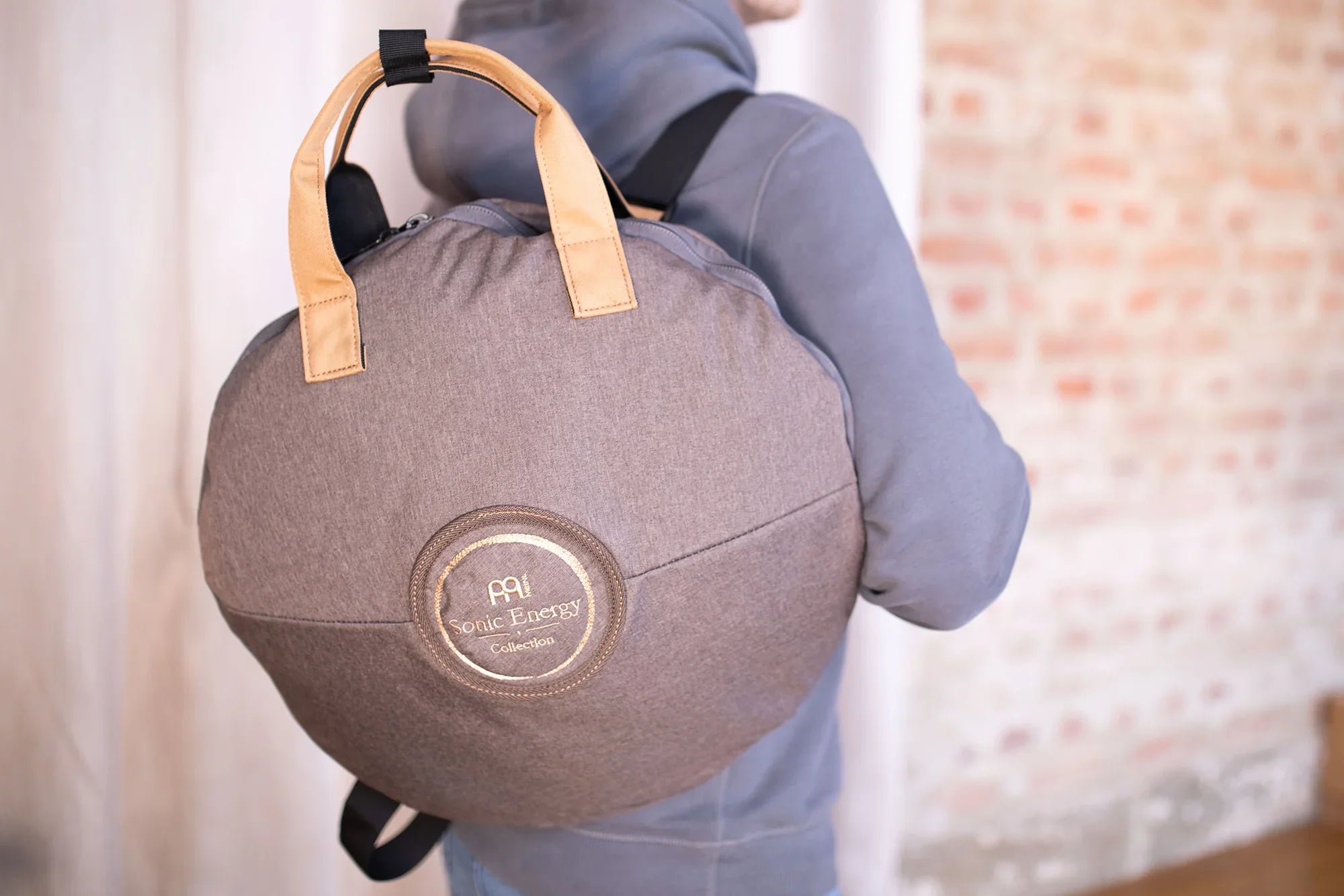 Person with round gray gong bag for sound healing instruments, leather handles, backpack straps