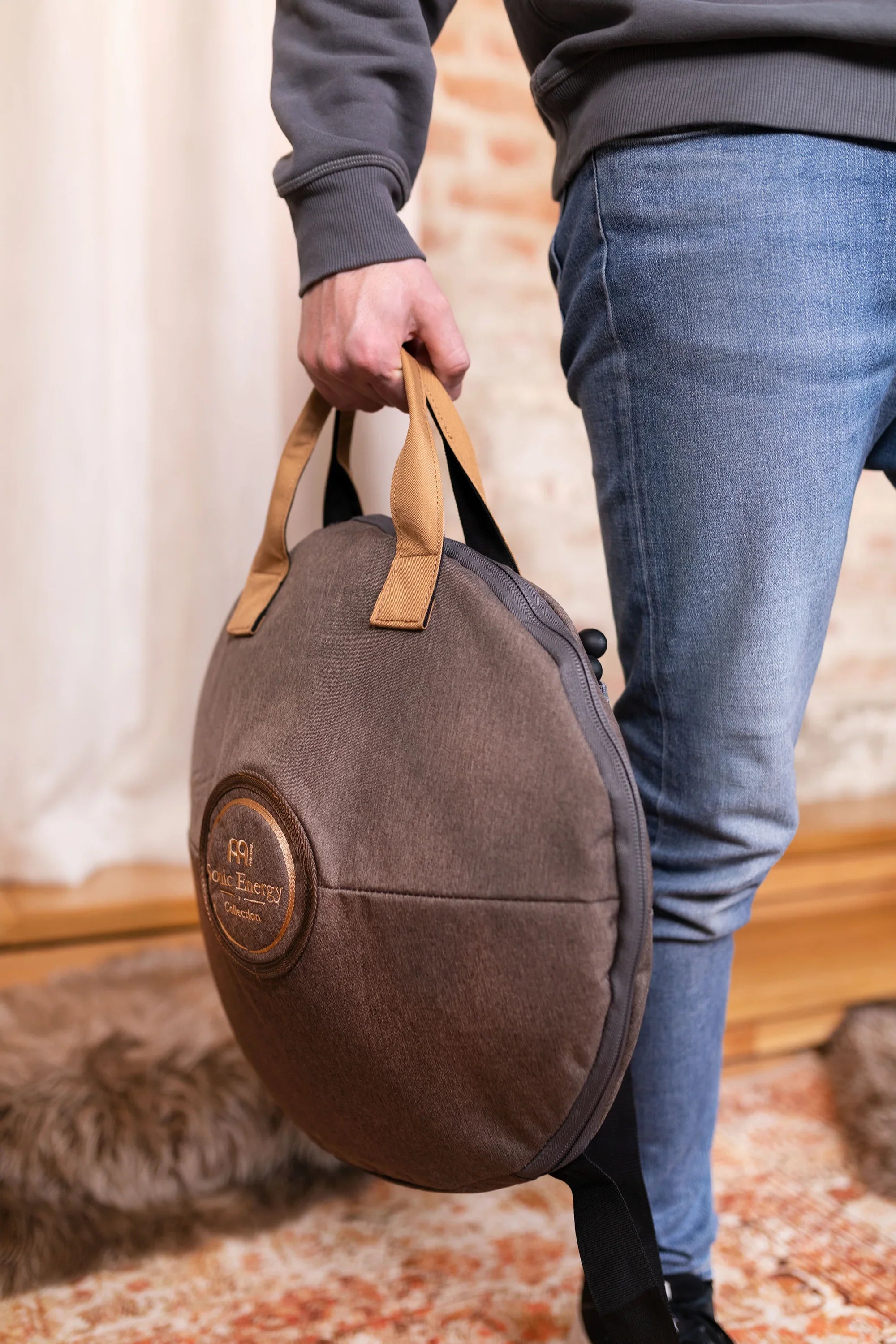 Person holding a round percussion instrument bag with tan handles indoors