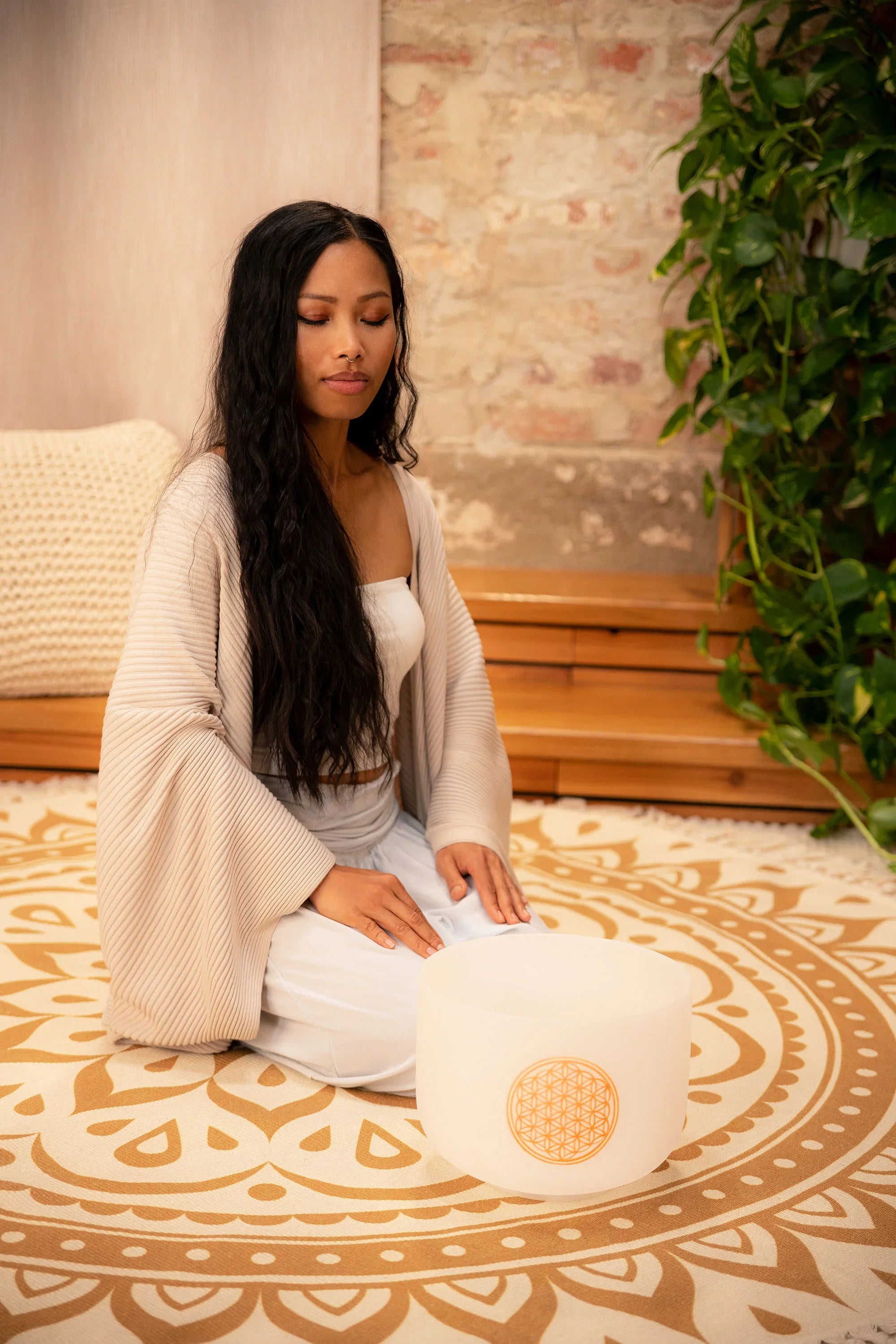 Woman meditating with crystal singing bowl on patterned mat for sound healing