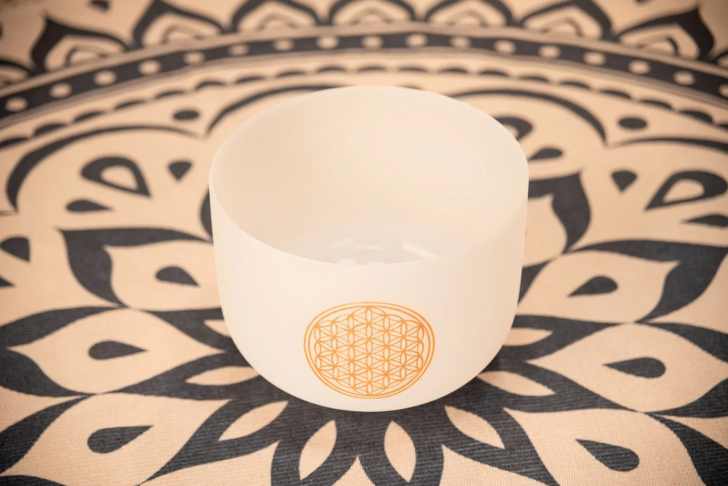 White crystal singing bowl with gold flower of life design on a patterned mat for sound healing