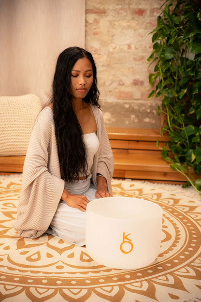 Woman meditating beside a crystal singing bowl on a mandala mat, sound healing setting