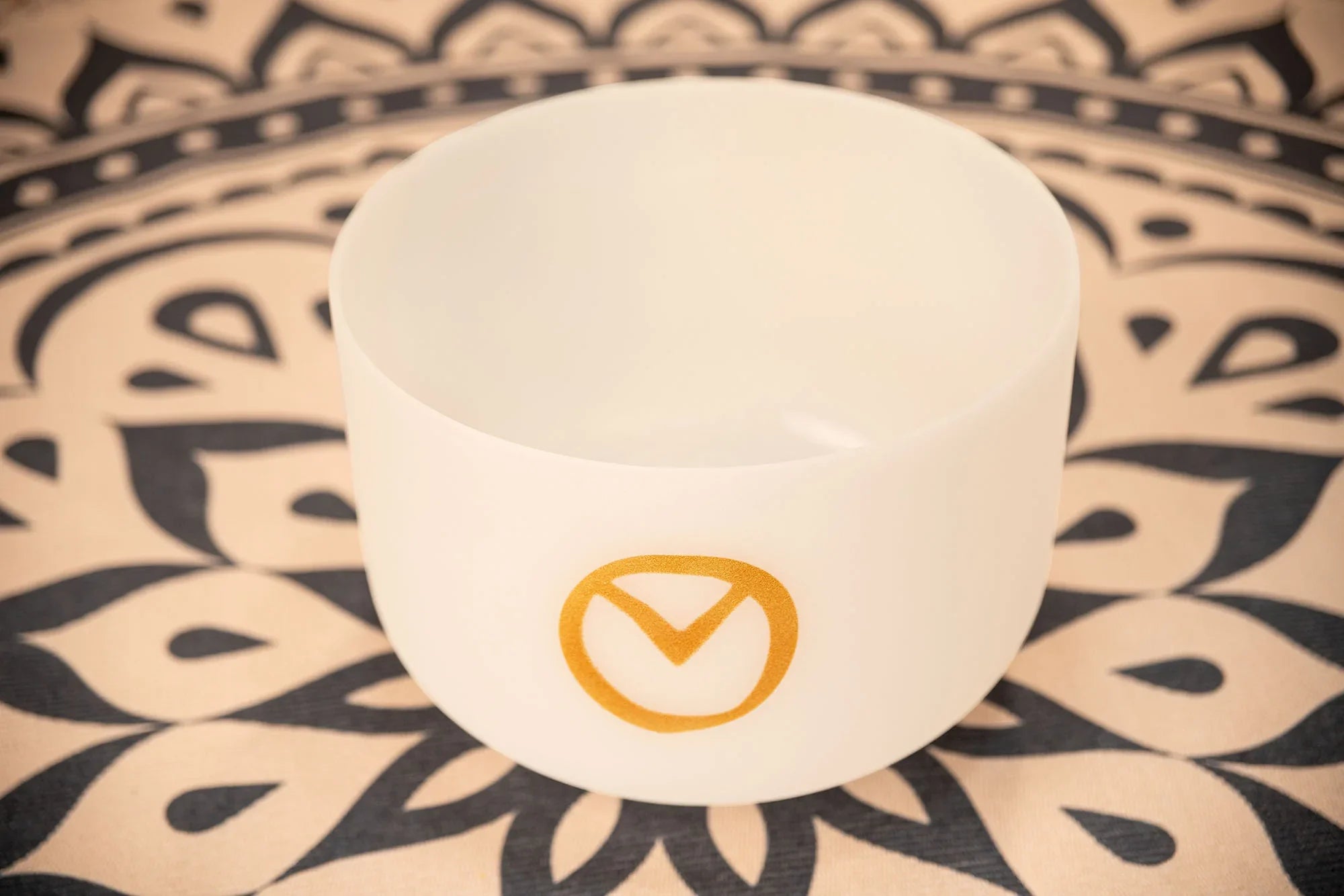 White crystal singing bowl with gold symbol on patterned yoga mat, sound healing instrument