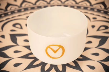 White crystal singing bowl with gold symbol on patterned yoga mat, sound healing instrument