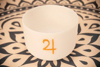 White crystal singing bowl with gold symbol on patterned mat for sound healing