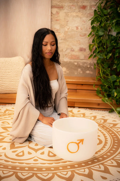Woman meditating indoors with crystal singing bowl for sound healing on patterned mat