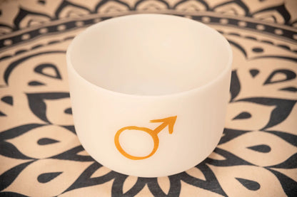 White crystal singing bowl with gold Mars symbol on patterned mat
