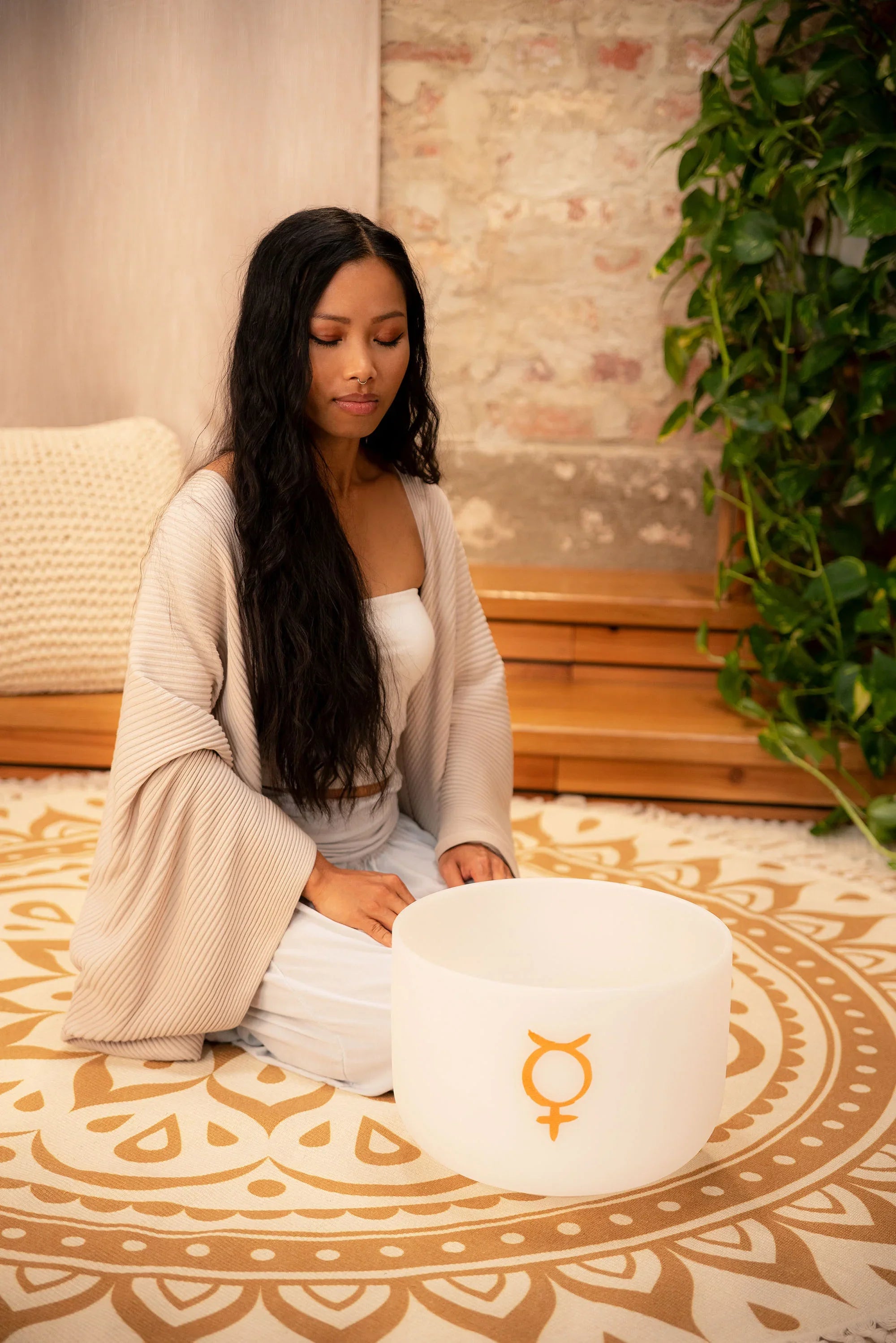 Woman meditating with a frosted crystal singing bowl for sound healing on patterned mat