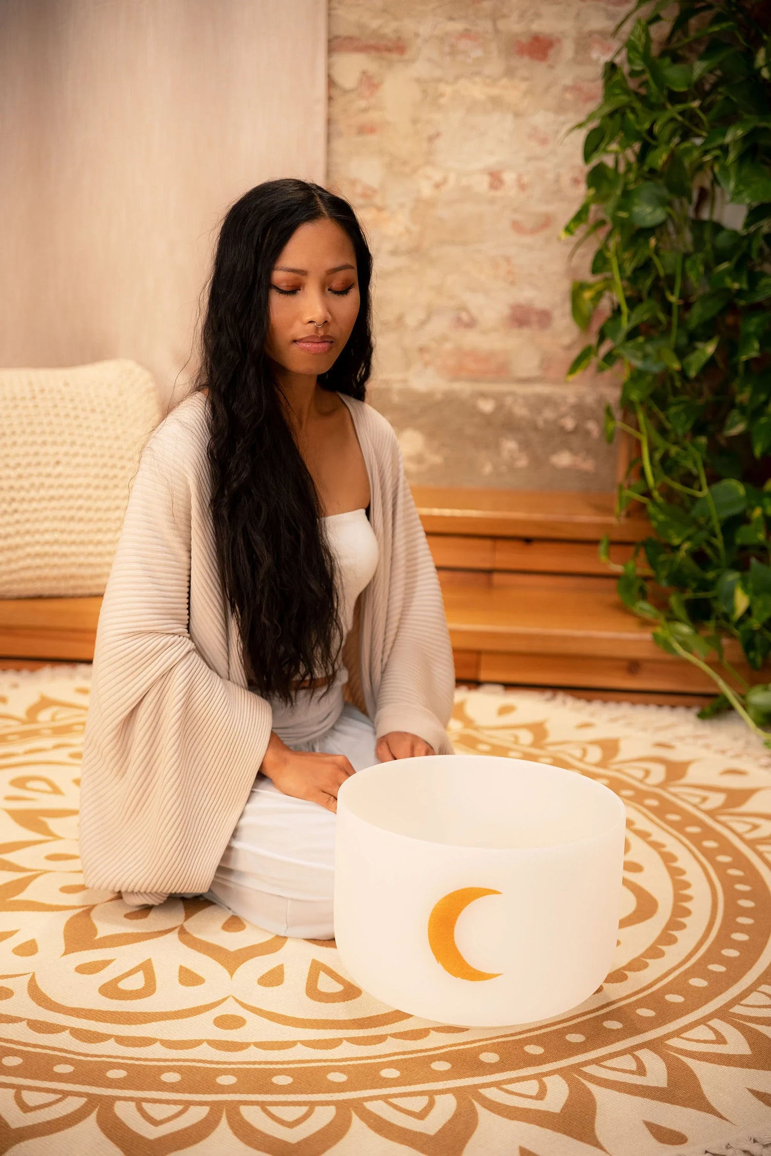 Woman meditating with a crystal singing bowl on a mandala mat in a peaceful room