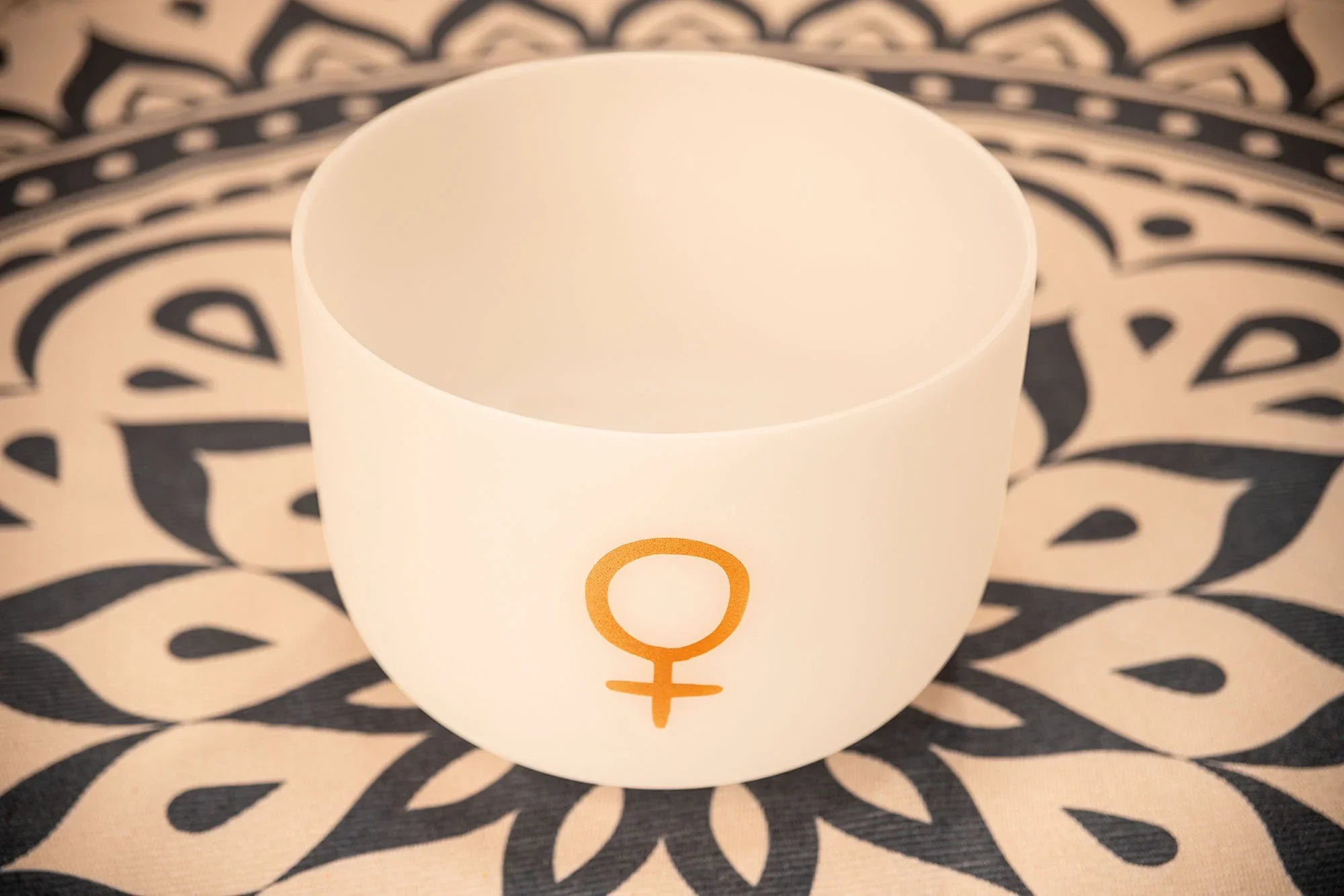 White crystal singing bowl with gold Venus symbol on a patterned mat