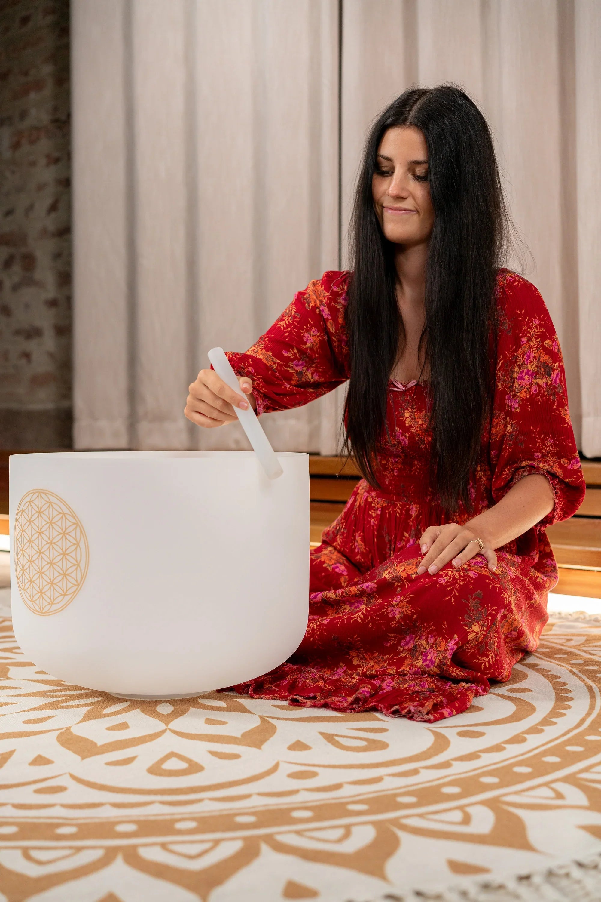 Woman in red dress playing a white crystal singing bowl for sound healing indoors