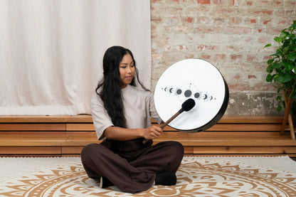 Woman playing a moon phase shamanic drum for sound healing indoors