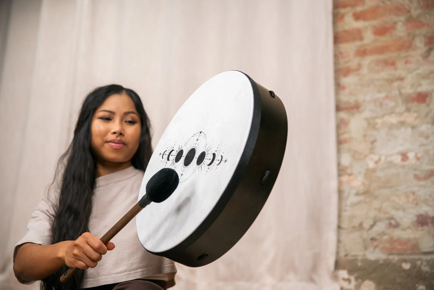 Woman playing a round frame drum with moon phase design for sound healing indoors