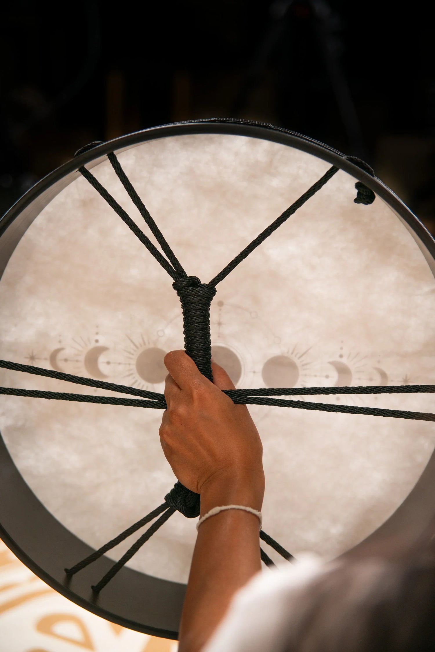 Hand holding a shamanic frame drum with moon phase design, energy healing instrument