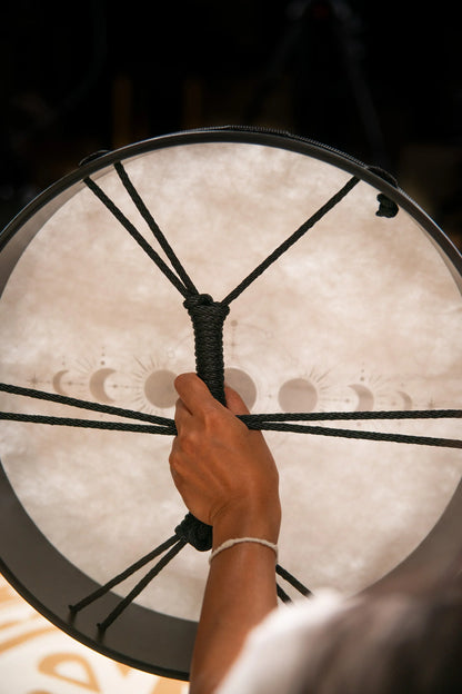 Hand holding a shamanic frame drum with moon phase design, energy healing instrument