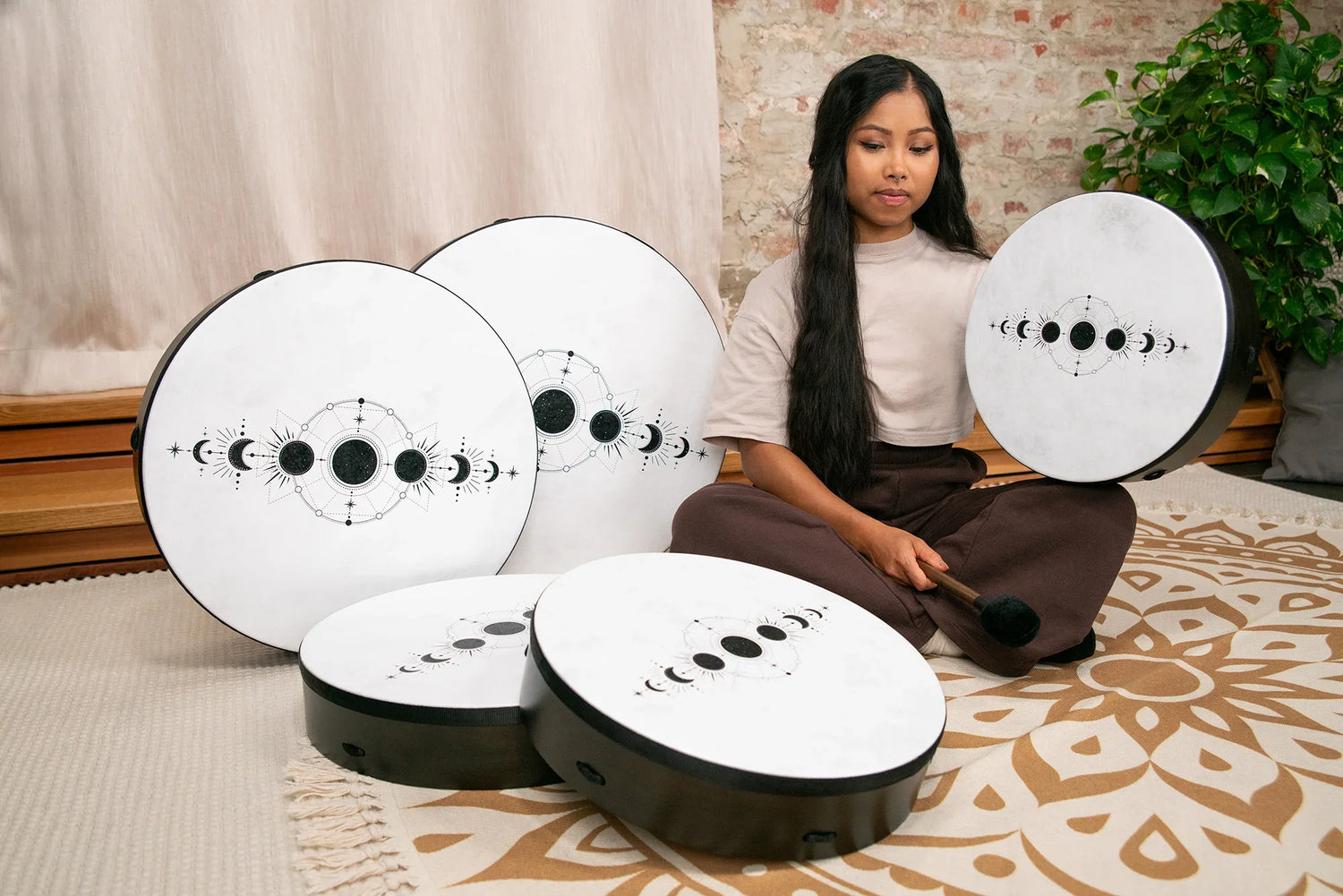 Woman playing large white frame drums with moon phase designs for sound healing