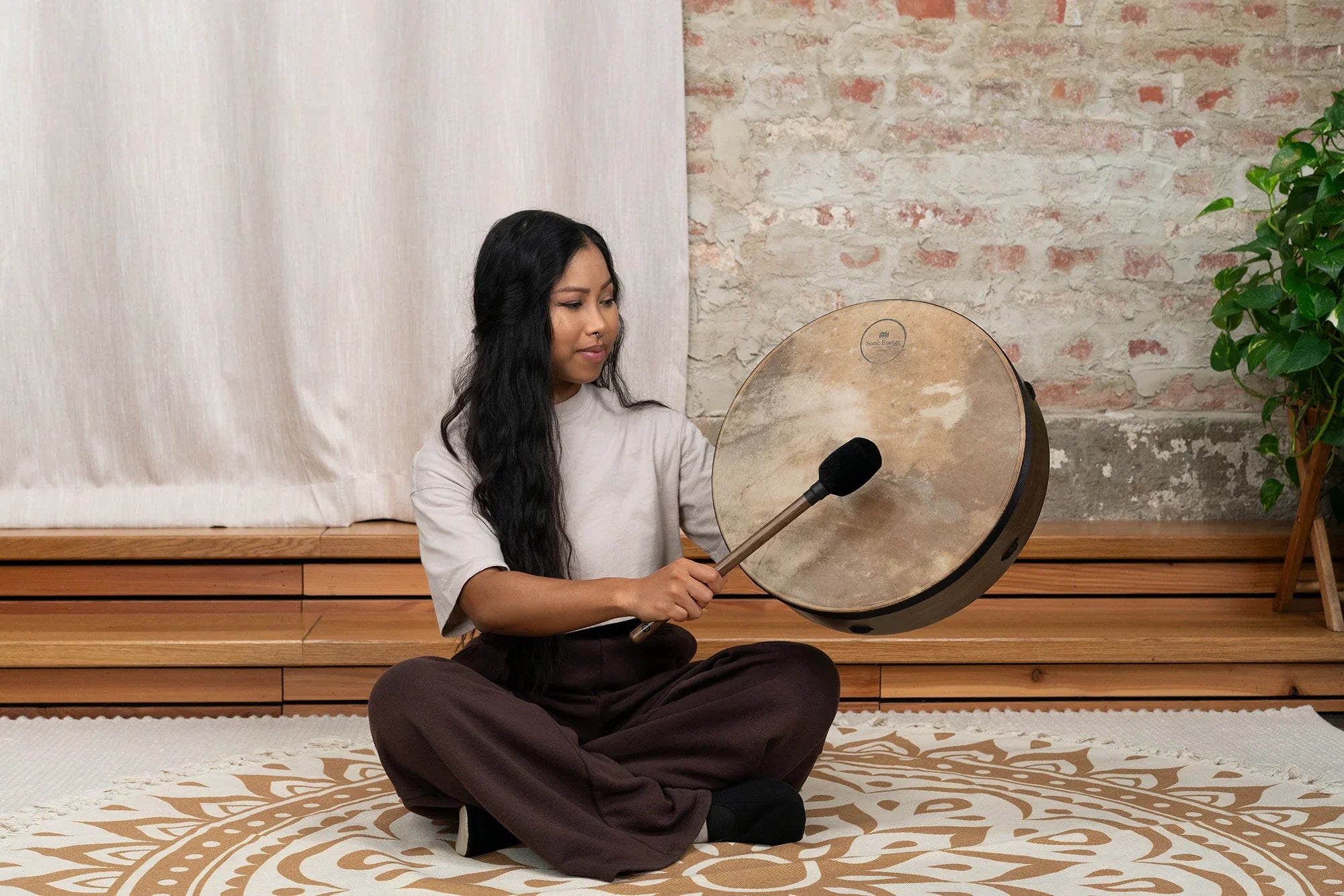 Woman playing hand drum for sound healing meditation on patterned mat indoors