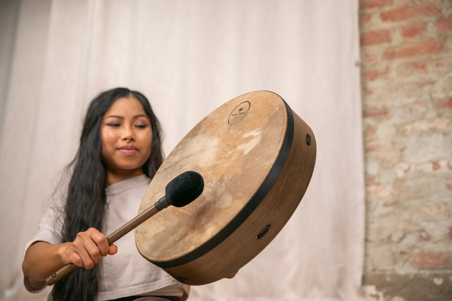 Woman playing frame drum with mallet for sound healing indoors