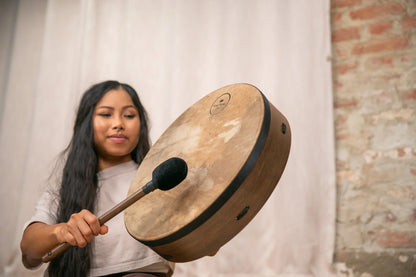 Woman playing frame drum with mallet for sound healing indoors