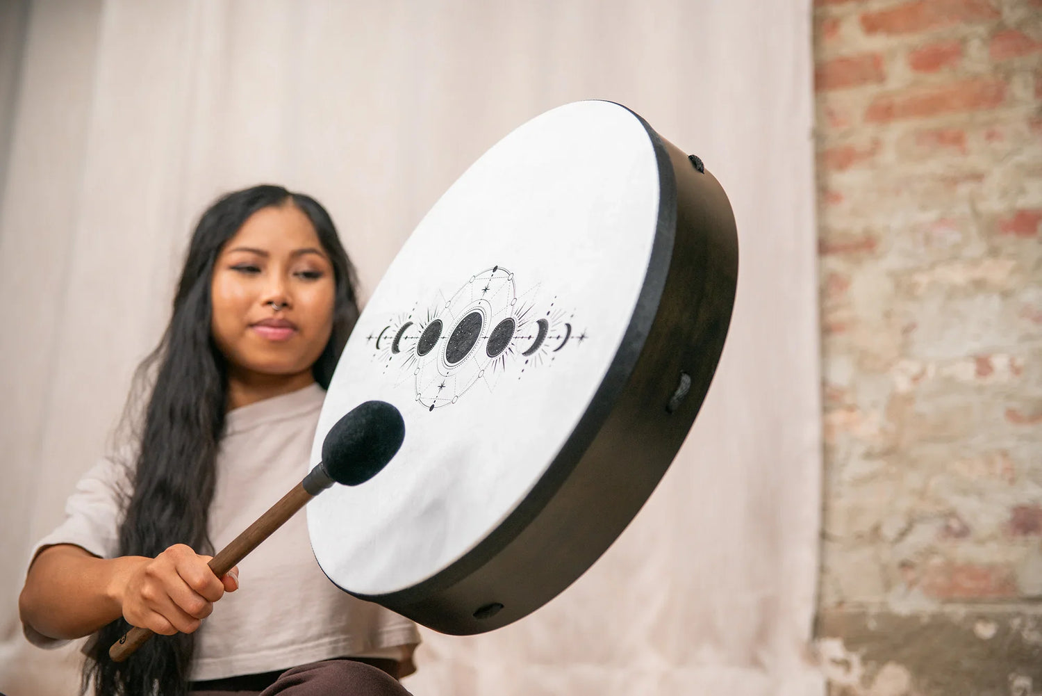 Woman playing a hand drum with moon phase design, energy healing instrument indoors