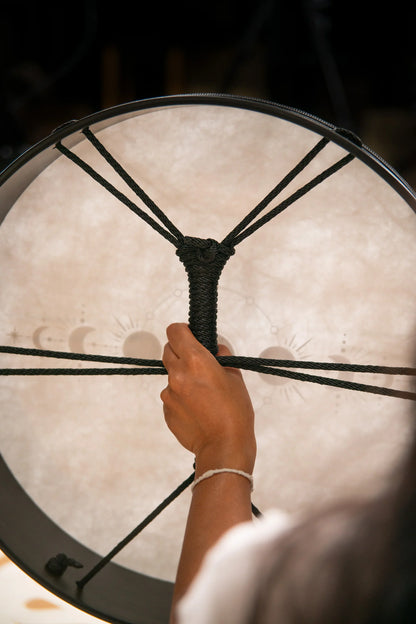 Hand holding rope handle of a healing frame drum with moon phase symbols.