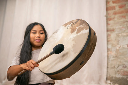 Woman playing a large hand drum with a mallet in a relaxed indoor setting