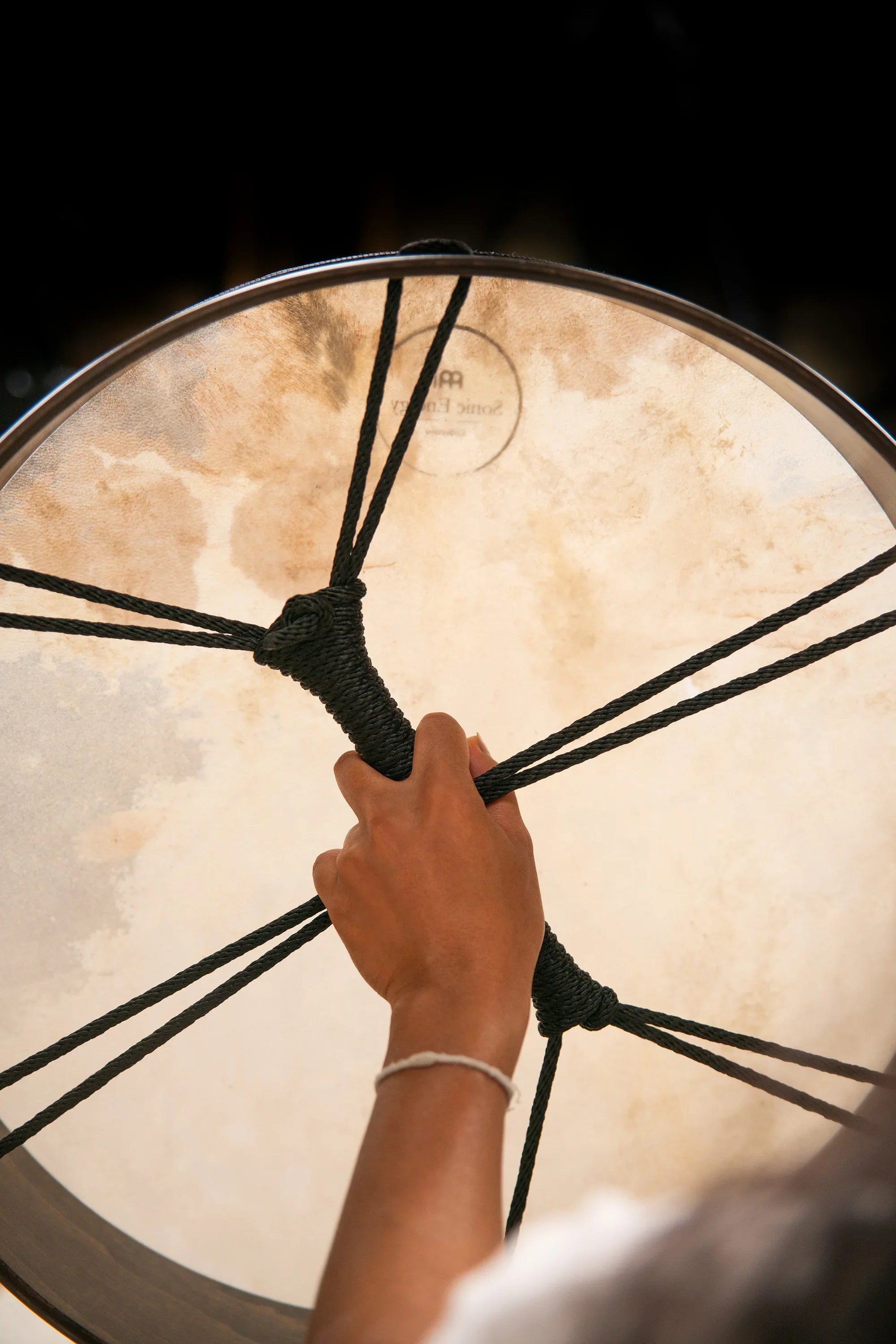 Hand holding a large frame drum with rope handle, used for sound healing or meditation.