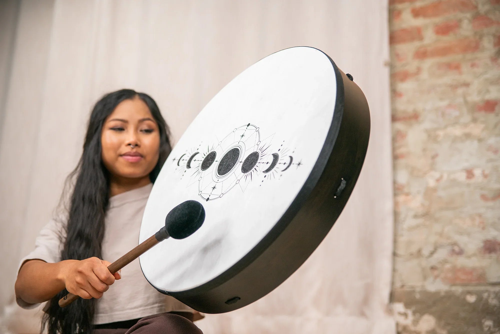 Woman playing frame drum with moon phase design for sound healing indoors
