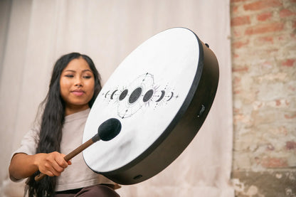 Woman playing frame drum with moon phase design for sound healing indoors